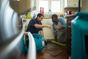 ServiceMaster Restore tech talking to homeowner and using pump to mitigate water from a kitchen